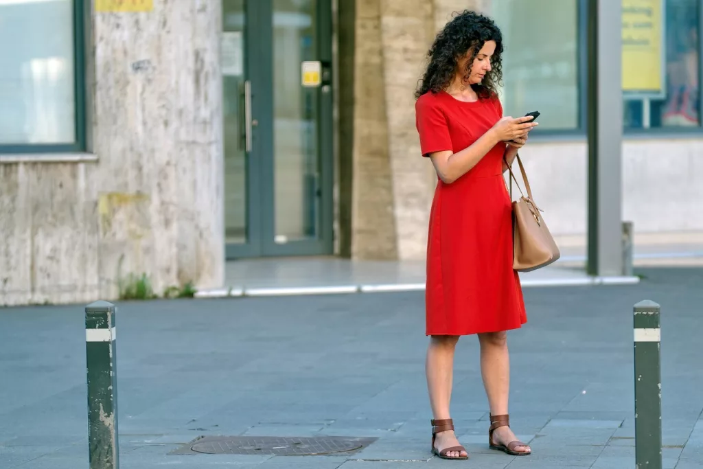 A woman checking her phone on a sunny city street while adjusting to a new culture