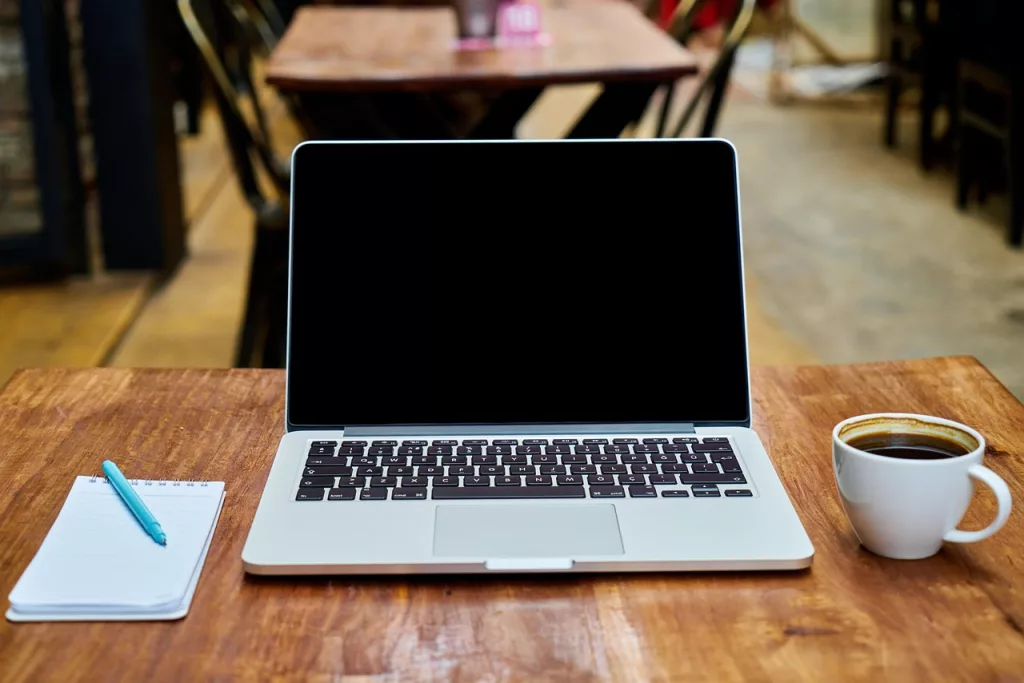 A laptop, notebook and coffee on a bright cafe table for journaling abroad